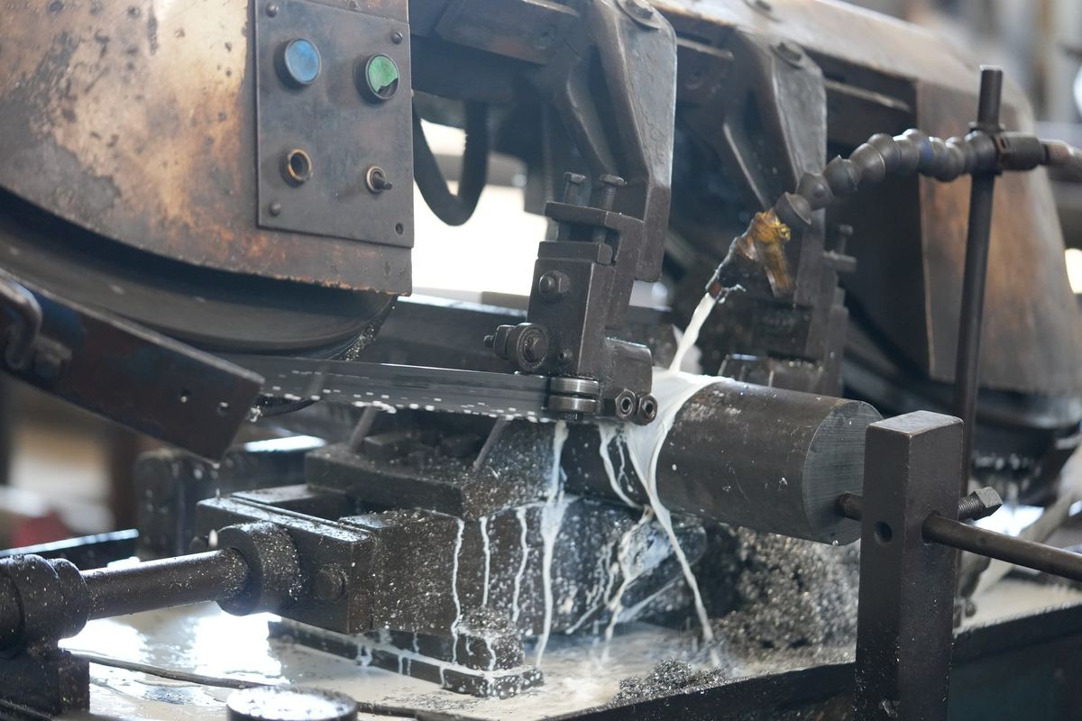 Band saw cutting a steel bar with coolant flowing over the blade