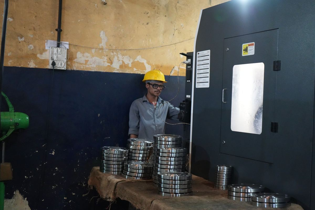 Operator at a CNC lathe with stacks of machined stainless flanges on the bench
