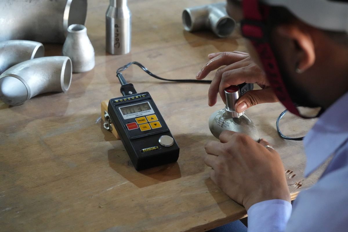 Inspector measuring wall thickness of stainless fittings with an ultrasonic gauge